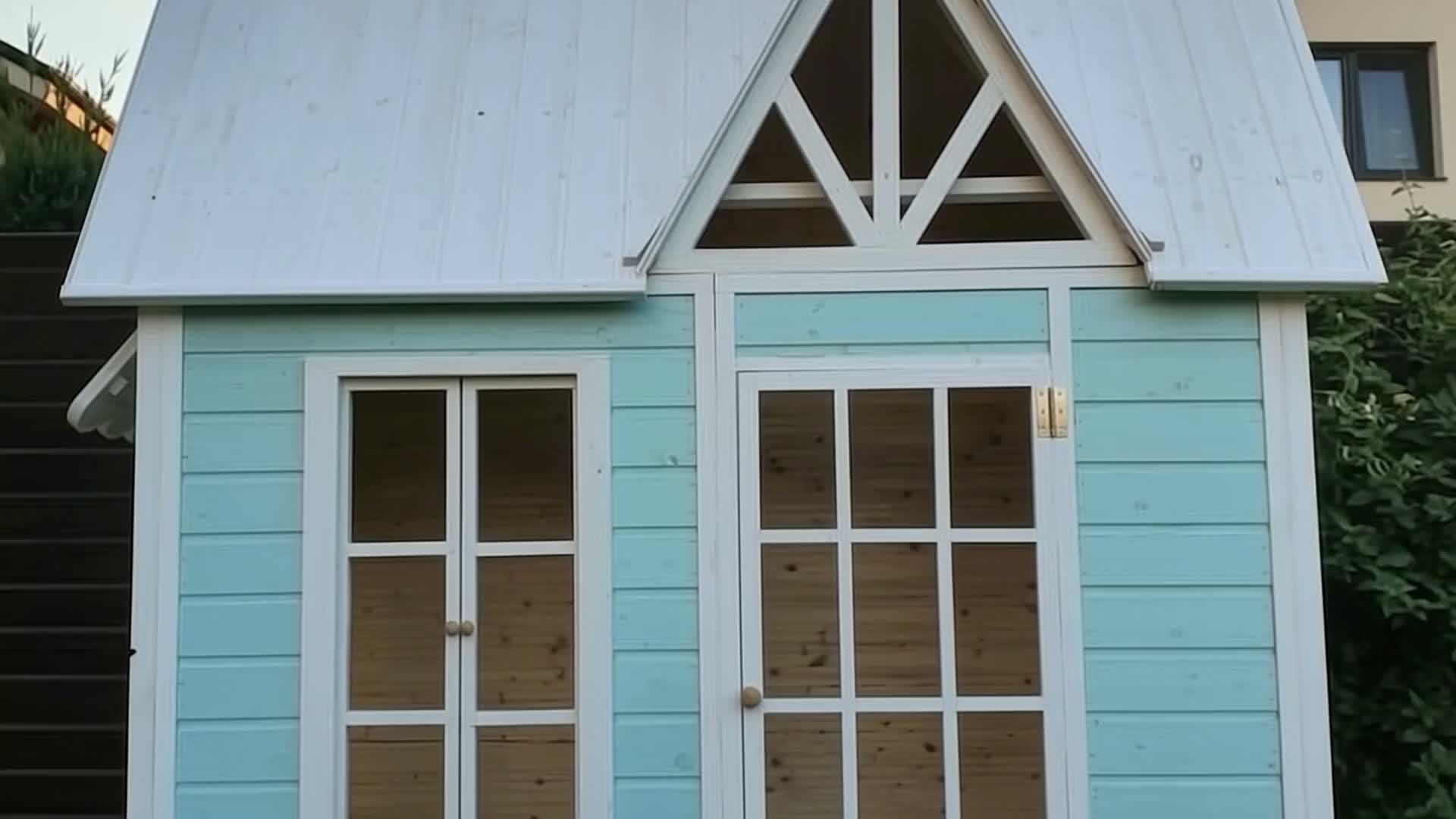 Straight-on view of a pale aqua playhouse with a steep white roof and glazed door